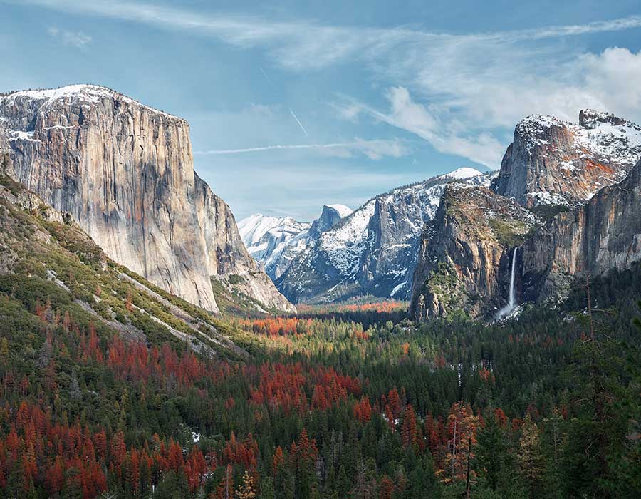 Yosemite National Park's majestic El Capitan and Bridalveil Fall with vibrant autumn foliage and snow-capped peaks in the distance.