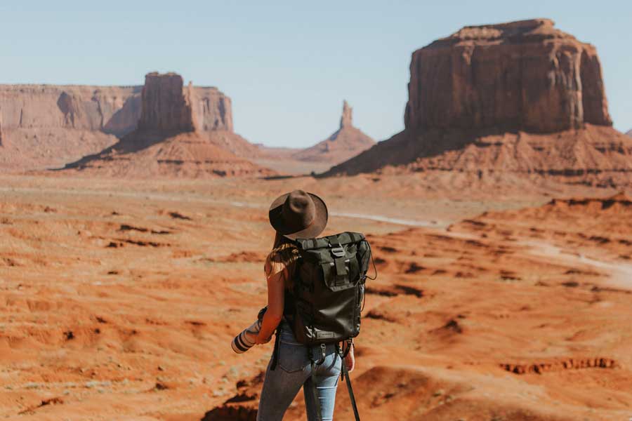 Traveler explores the iconic red mesas of Monument Valley under a clear blue sky.