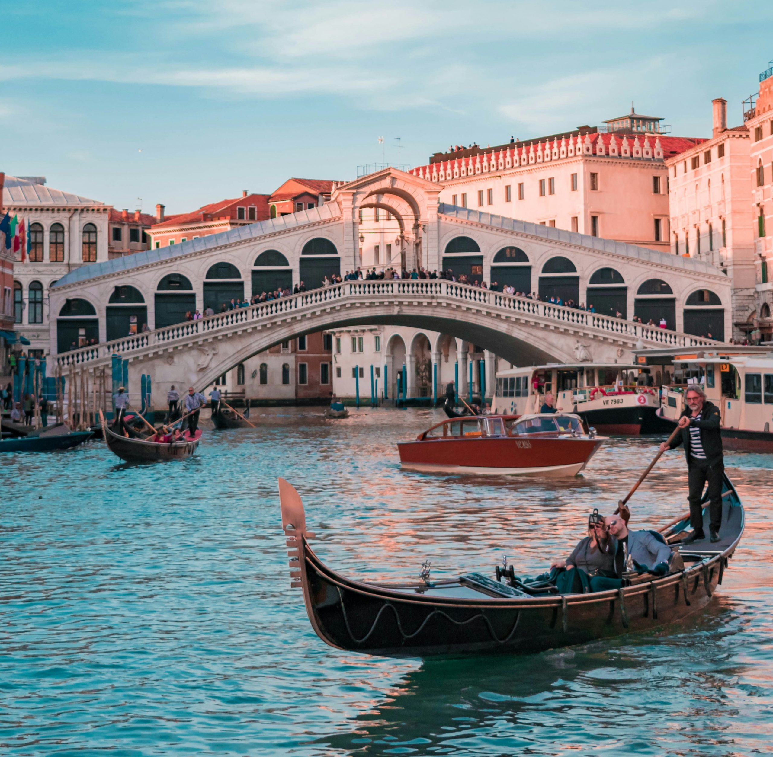 Gondolas glide under the Rialto Bridge on Venice's scenic Grand Canal at sunset.