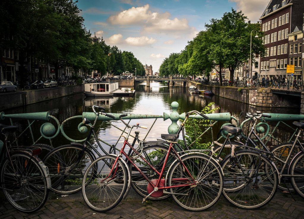 Charming Amsterdam canal view with bicycles lined up on a bridge, showcasing the city's picturesque waterways and greenery.