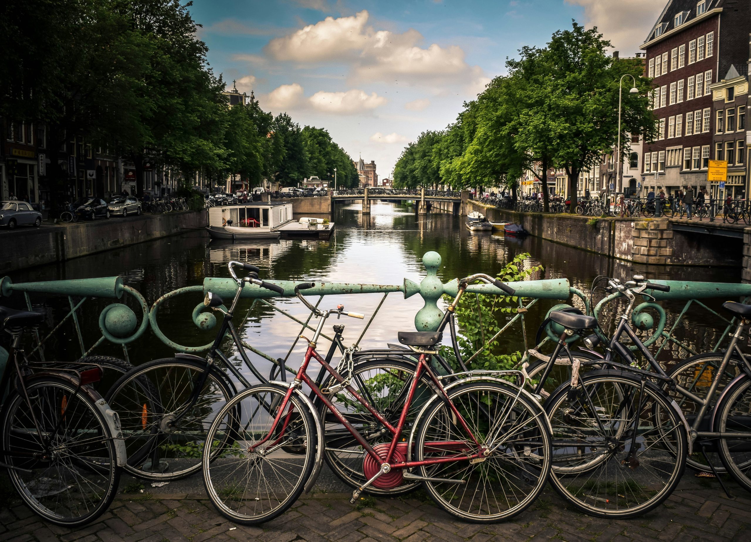 Charming Amsterdam canal view with bicycles lined up on a bridge, showcasing the city's picturesque waterways and greenery.