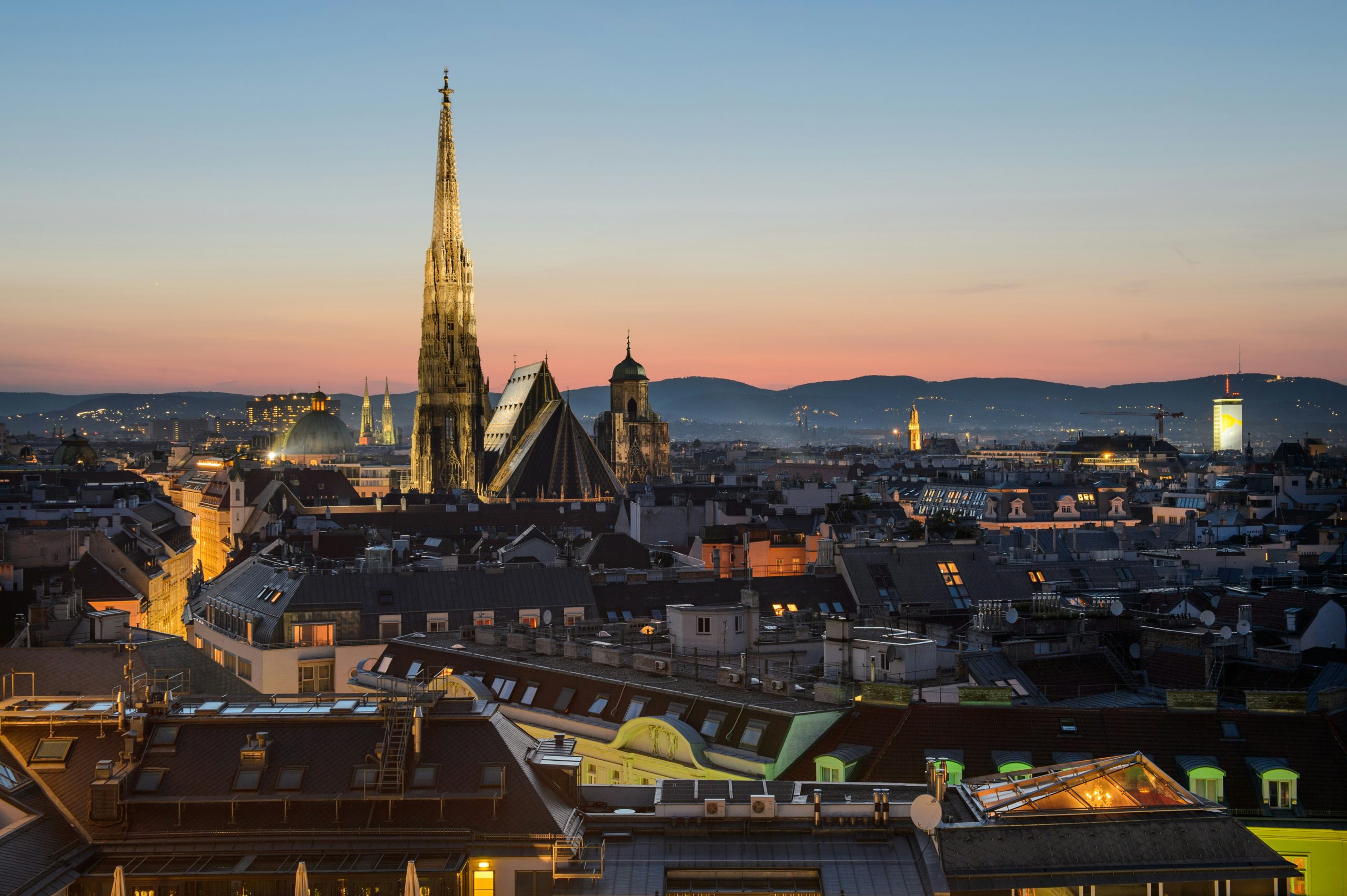 Vienna skyline at dusk, highlighting St. Stephen's Cathedral with a vibrant sunset backdrop and distant hills.