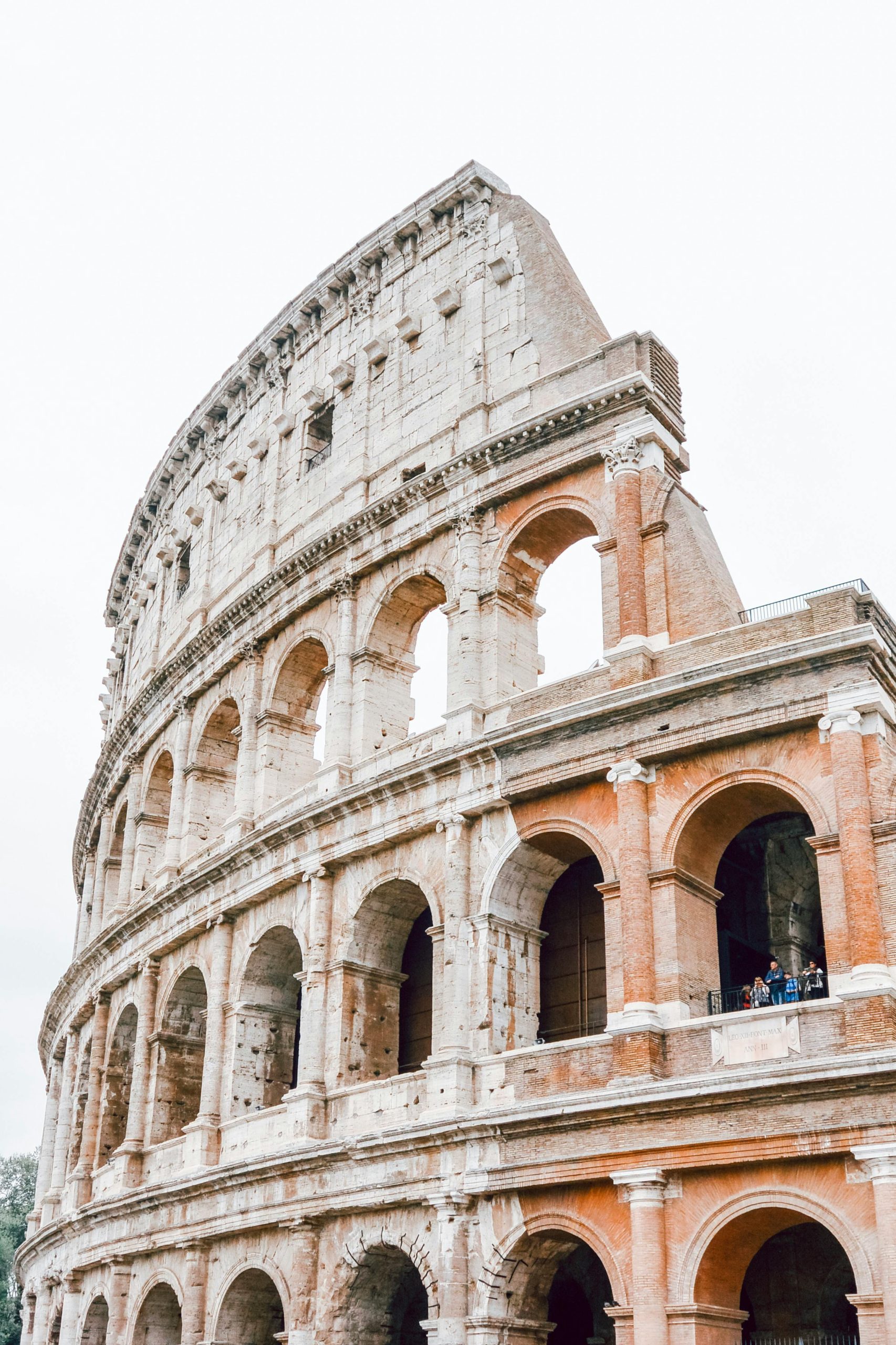 The Colosseum in Rome stands majestically against a pale sky, showcasing its ancient arches and historic grandeur.