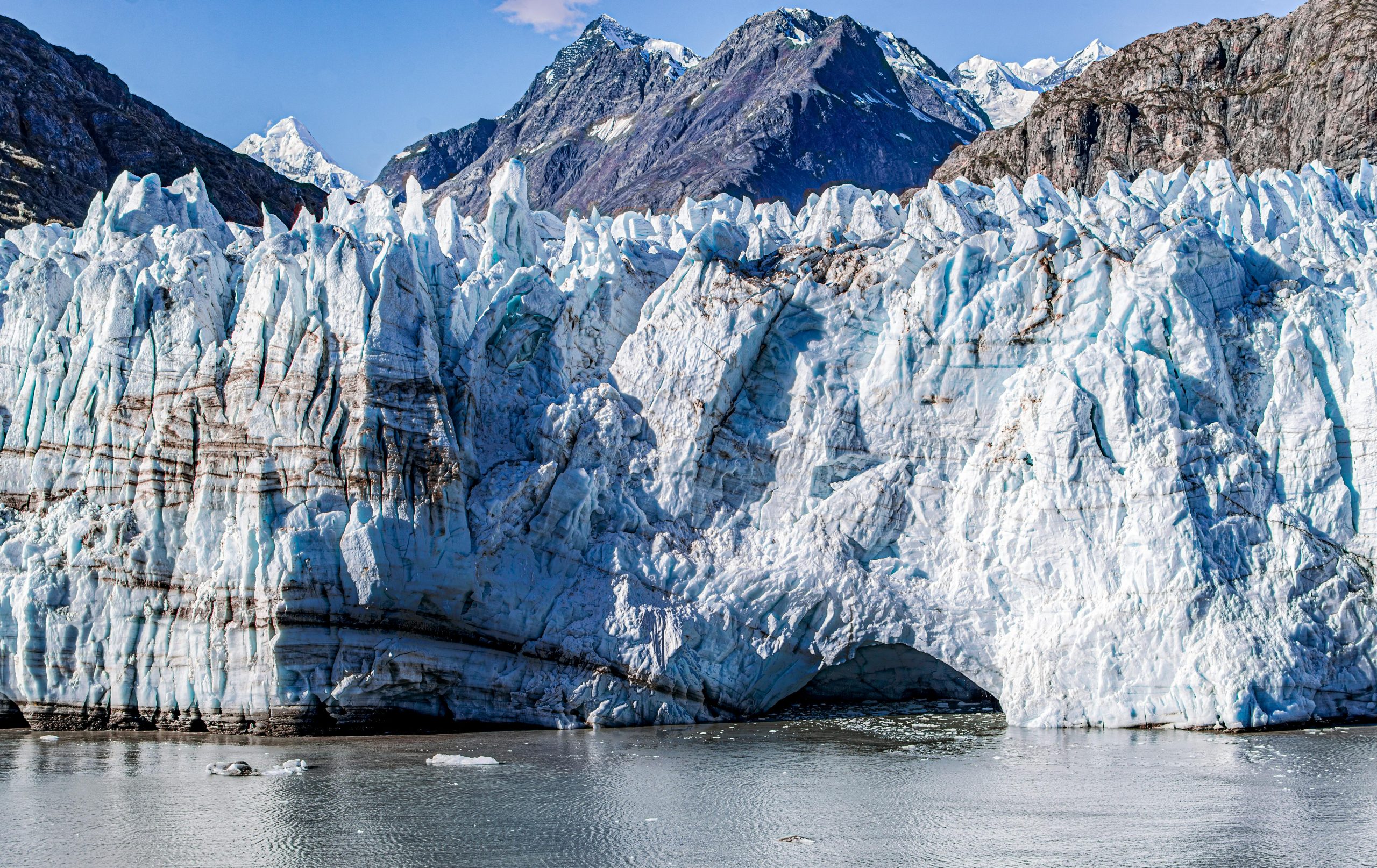 Massive blue glacier in Glacier Bay, Alaska, set against rugged peaks under a clear sky.