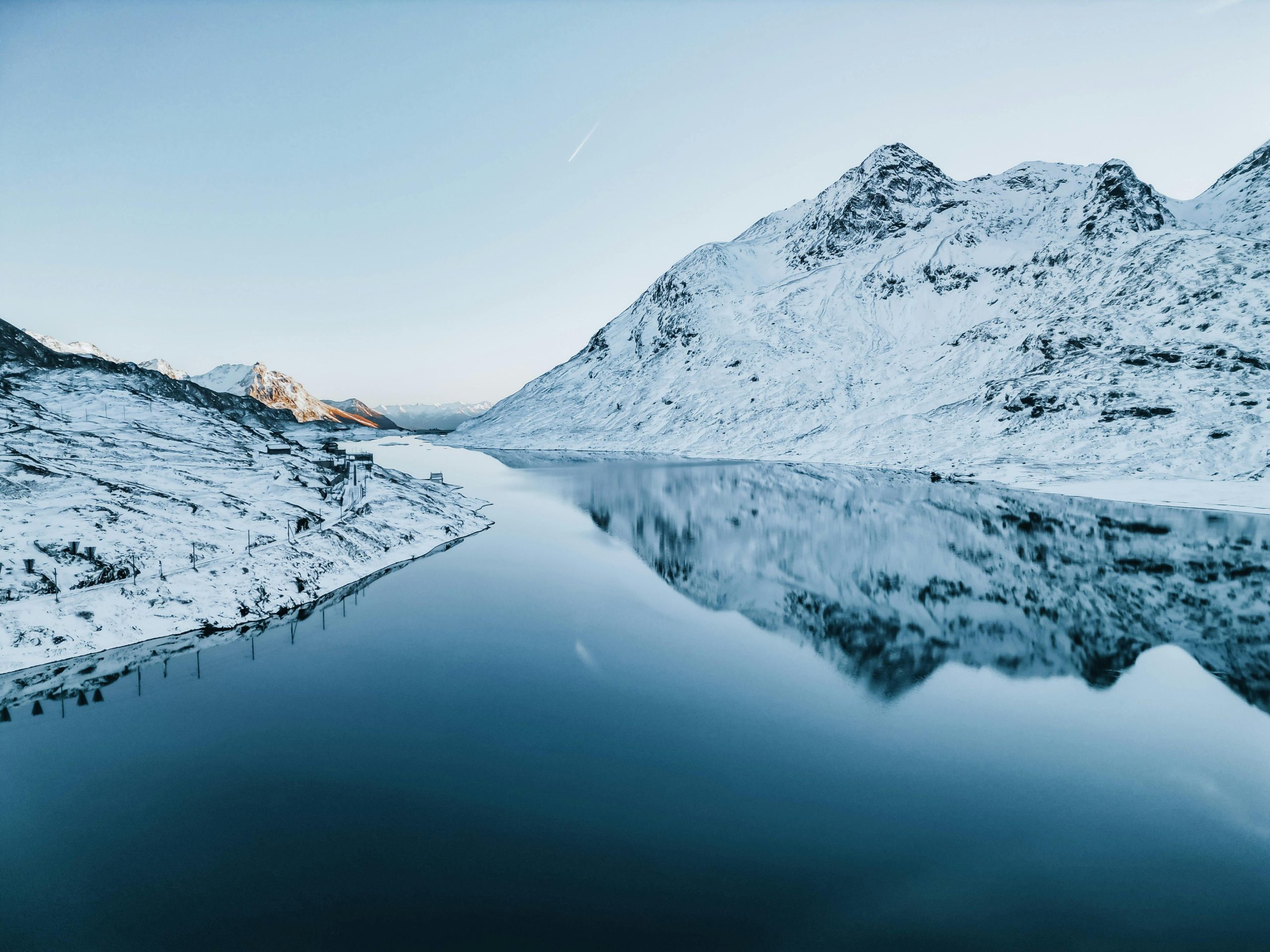 Snowy Swiss Alps reflecting in a serene lake at dawn, offering a tranquil and picturesque winter escape.