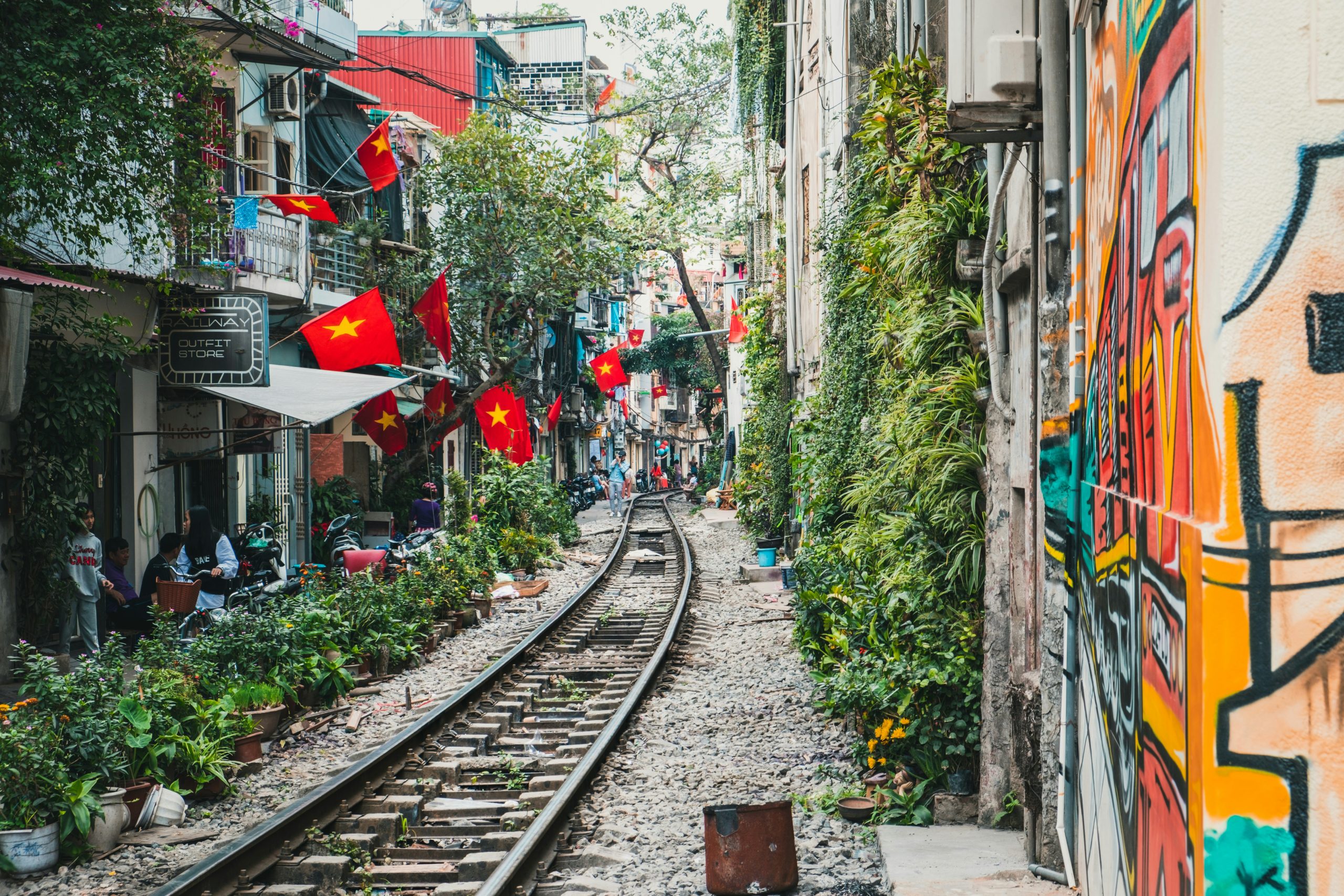 Vibrant Hanoi street with train tracks, lush greenery, and Vietnamese flags creating a unique urban landscape.